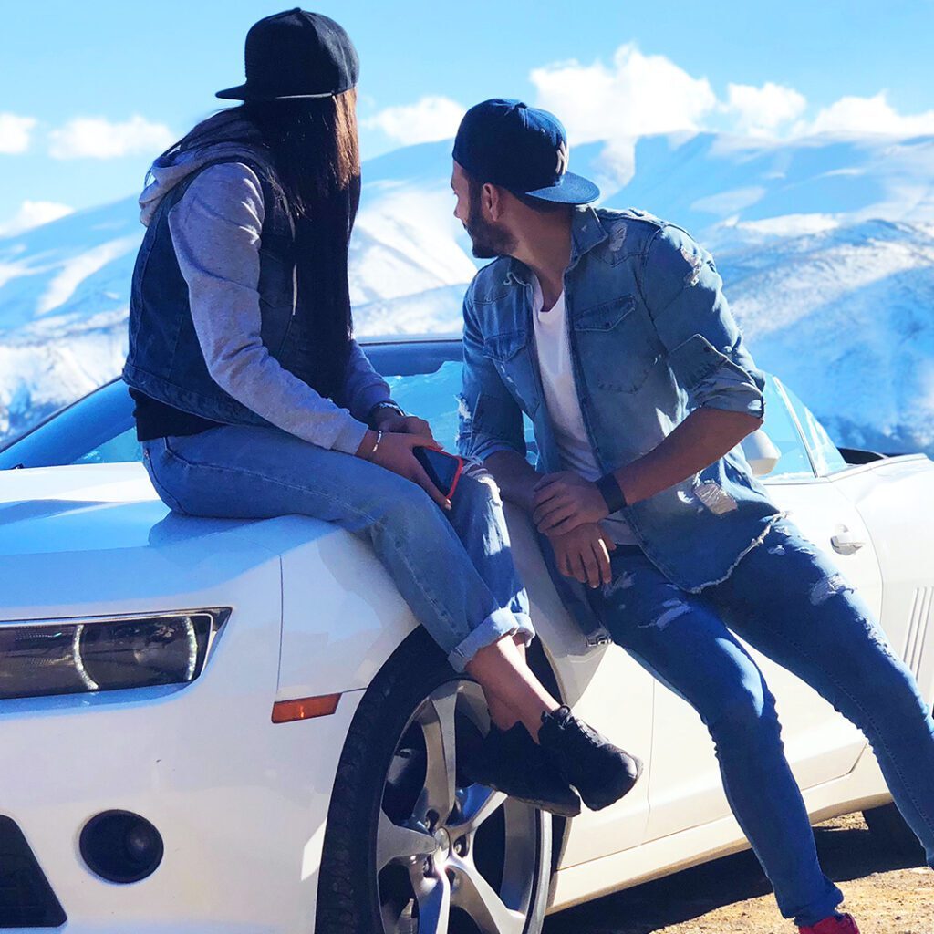 Couple on white Camaro convertible with snowy mountains.
